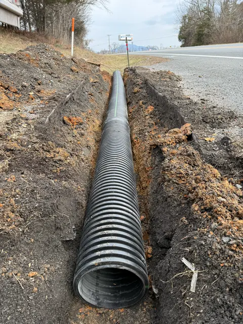 Large corrugated culvert pipe bedded in an open trench beside a rural road.