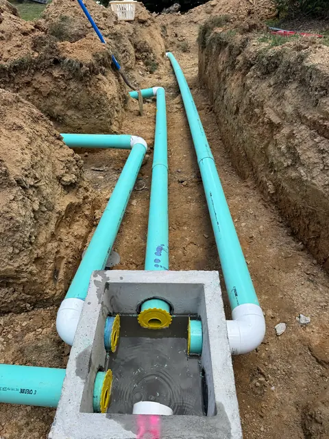 Green PVC sewer laterals running to a concrete junction box in an open trench.