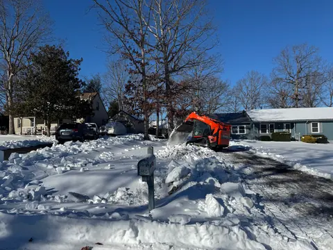 Orange Kubota track loader pushing snow off a residential driveway.